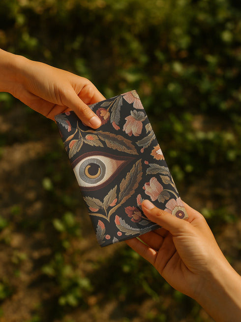Set of four square black polyester cloth napkins featuring a central embroidered-style eye motif framed by floral and leaf patterns in autumnal tones of rust, ochre, and gold. The design is printed on one side, with a white reverse. Each napkin measures 18x18 inches.